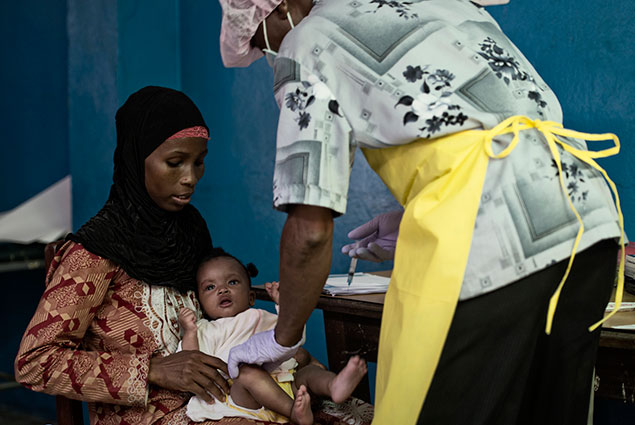 A mother holds her baby while a health worker administers a shot.