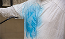 Close up of person wearing white medical suit with blue liquid being sprayed onto chest. Credit: http://www.ebolagrandchallenge.net