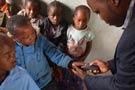 A doctor uses a device on a young boy with other children looking on