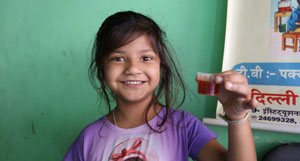 A young girl holds up a vial of a red liquid