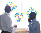 Two men look at post-it notes on a white board