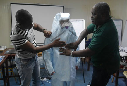 Two men help put protective clothing on a third person.
