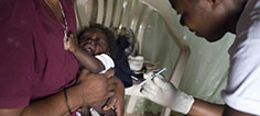 A woman holds a baby while she gets her immunizations