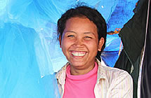 A woman smiles from beneath mosquito nets