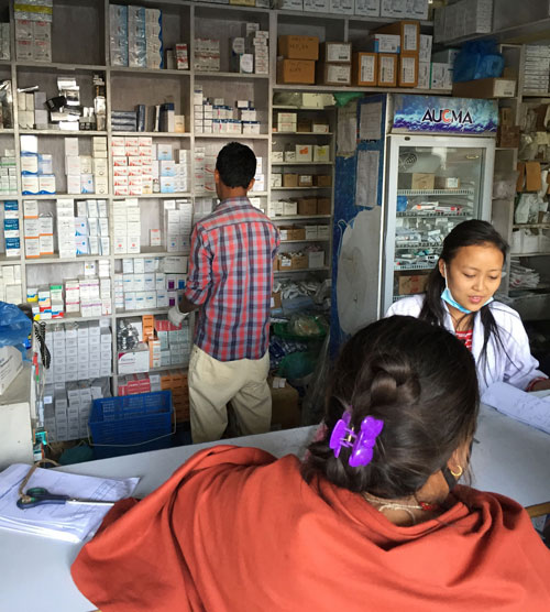 A pharmacist stands at a wall of medicine.