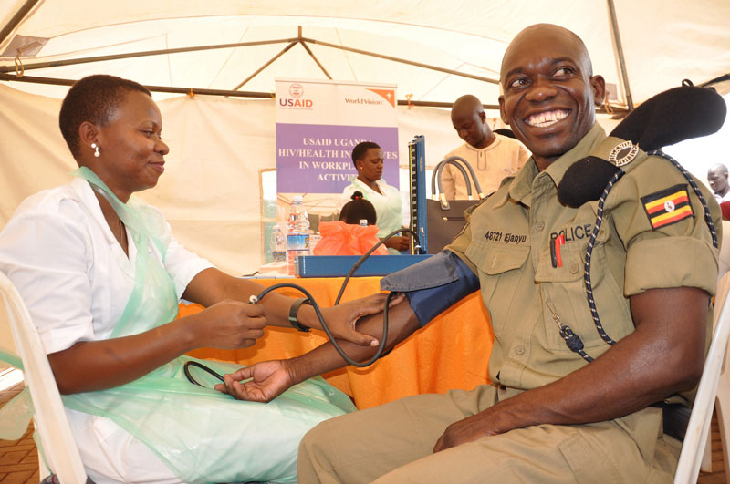 A health care worker takes the blood pressure reading from a smiling local police officer at a USAID sponsored event. Photo credit: HIWA