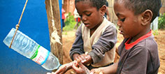Two children wash their hands from a tipping water bottle