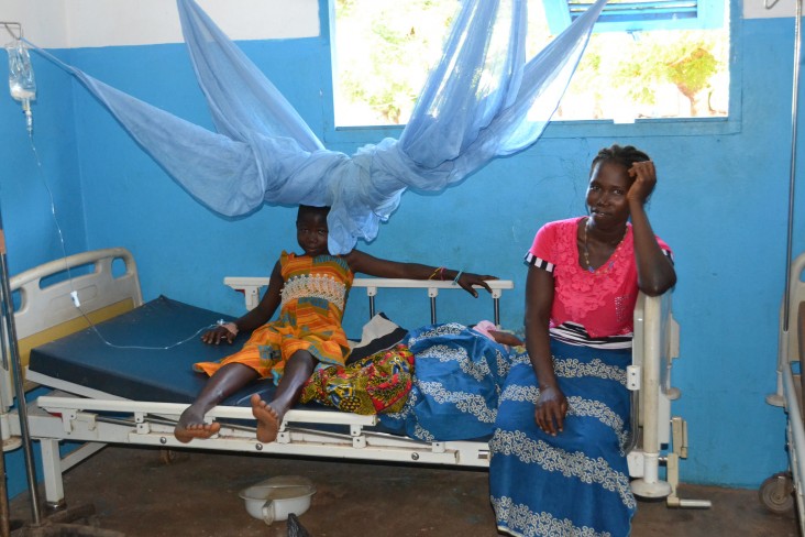 Une patiente souffrant du paludisme assise sur son lit d’hôpital à côté de sa mère.