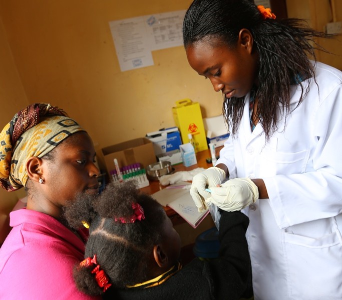 This image shows a medical technician in a clinic providing a service to a local child.