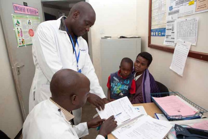 Two medical personnel review a patient's charts while the mother and her son look on.