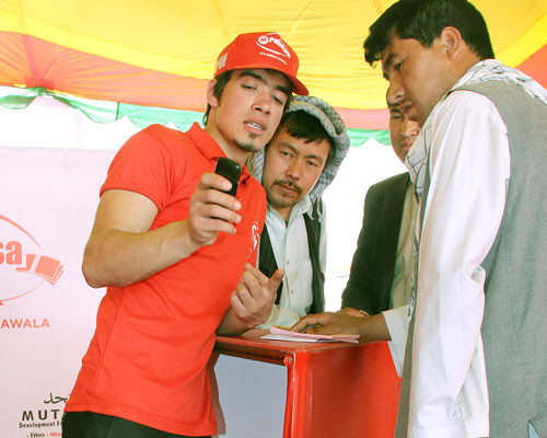 Several young Afghan men listen as a representative from M-Paisa describes how mobile bill pay works. 