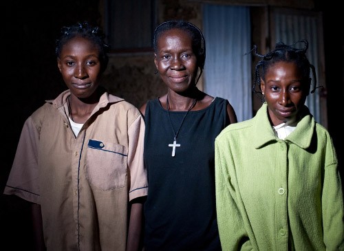 Florence, Rosalie, and Diane Ouedraogo stand outside their home on a cool evening.