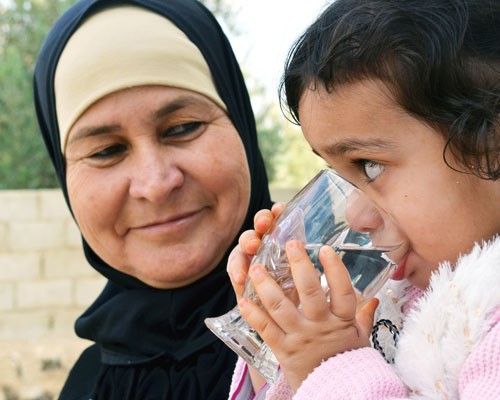 Al Khaldi’s 2-year-old granddaughter drinks from a glass as her grandmother looks on.