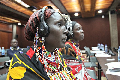 Kenyan women wearing their colorful traditional beads and fabrics wear headphones as they listen to a presentation.