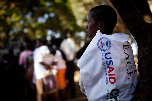 A Kenyan woman drapes herself with a USAID peace banner while she stands under the shade of a tree.
