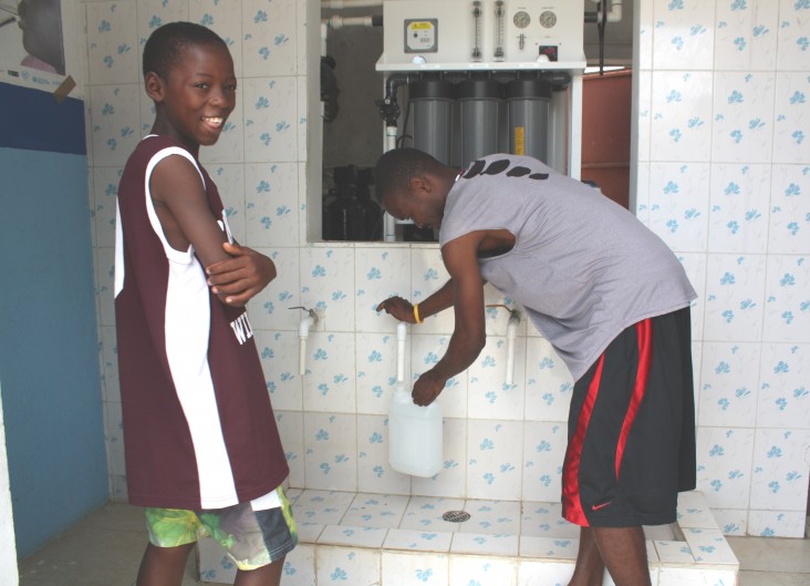 A boy buys clean drinking water from Pierre Ricardo at a reverse osmosis water treatment business in Caracol, Haiti.