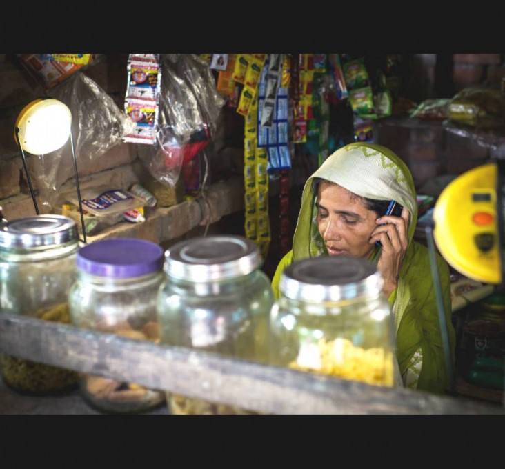 DCBS client Mamtaj Mondal in her shop lit by two solar lamps that can also charge her cell phone