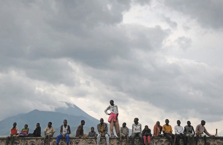 Men sit and stand atop a wall at a USAID help center next to a refugee camp on the outskirts of Goma.