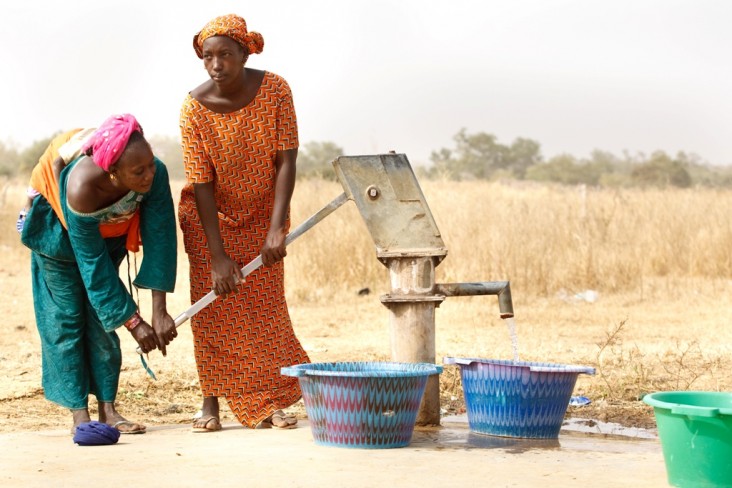 Two women pump water at a station