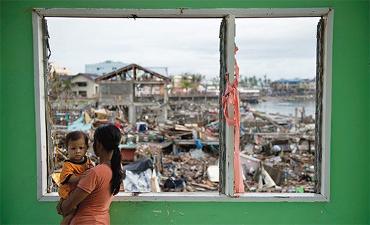 A victim from Typhoon Haiyan observes the devastated waterfront community in Tacloban. The Philippines loses up to $5 billion ev