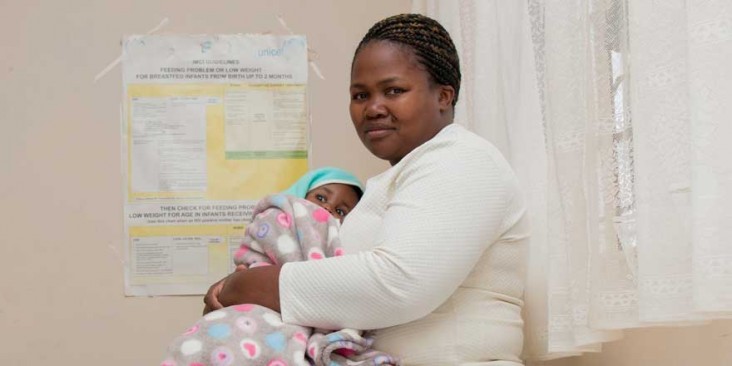 A mother holds her child in front of health posters.