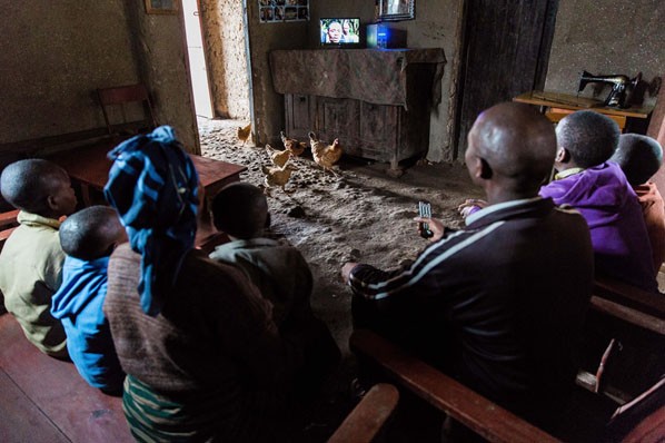 Andre and his family watching tv in their home. They recently purchased a solar power kit from BBOXX.