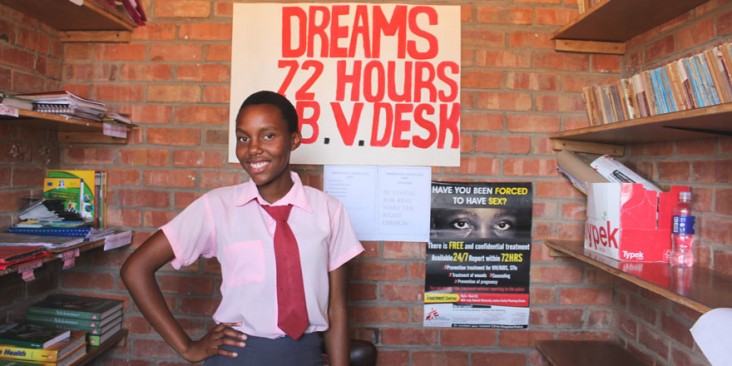 A young girl poses by a sign reading DREAMS 72 hours, b.v. desk