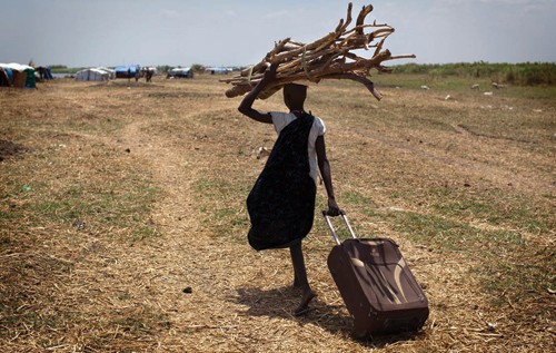 A South Sudanese woman walks with wood to reinforce her house in an isolated makeshift camp for internally displaced people in S