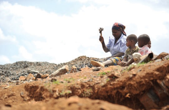 A Kenyan woman breaks stones for a local construction company at a quarry with her children. Women are more likely to be employe