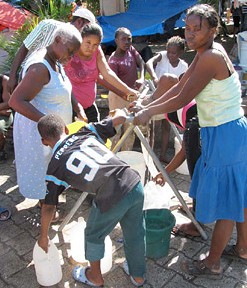 Camp residents filling water containers from a water-bladder fed tap stand.