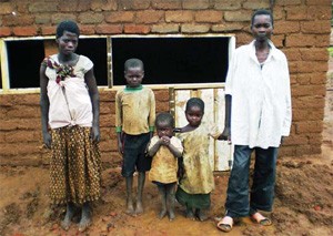 Vulnerable children spanning a range of ages stand in front of their village dwelling. 