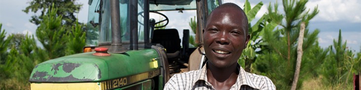 Small farmer Churchill Ojok stands with his tractor. Thanks to a USAID initiative, he is harvesting more efficiently. (Photo cou