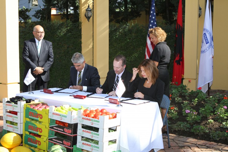 Three people sign a document at an outdoor ceremony