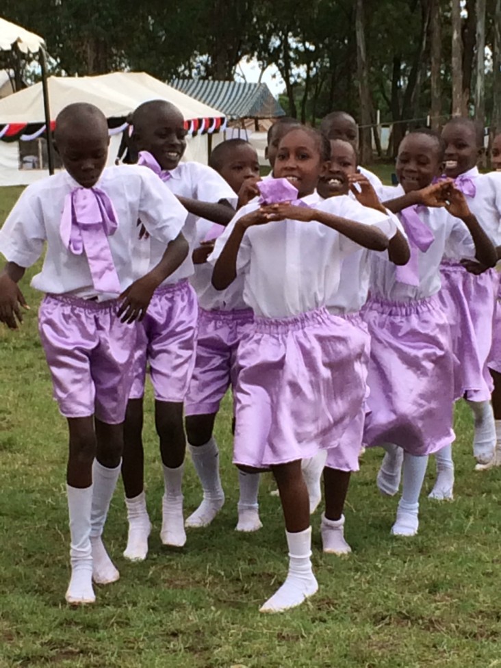 Two lines of Kenyan children wearing purple shorts march across a field