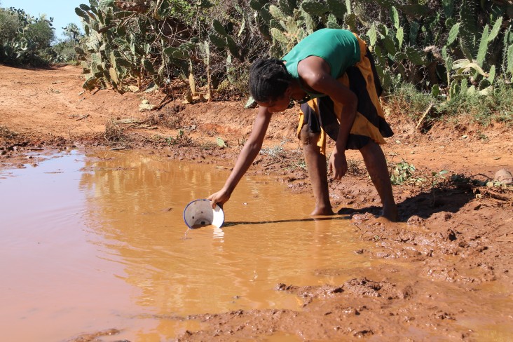 A child collects her family’s drinking water from a muddy puddle in the middle of the road