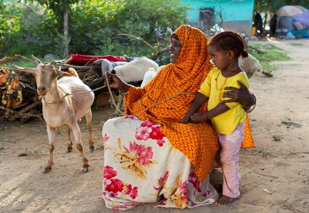 A mother, with child tend to her goat 