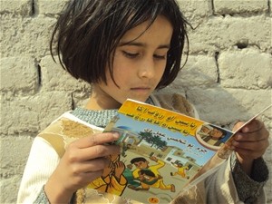 A school girl reads a USAID information comic book about the illegal use of the traditional conflict resolution practice of Baad