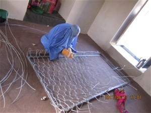 Afghan Gul weaves wire on a gabion cage in a community building near her home.