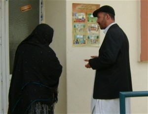 Using an Access to Justice Campaign poster, a USAID worker explains women’s right to inheritance to a woman entering a health cl