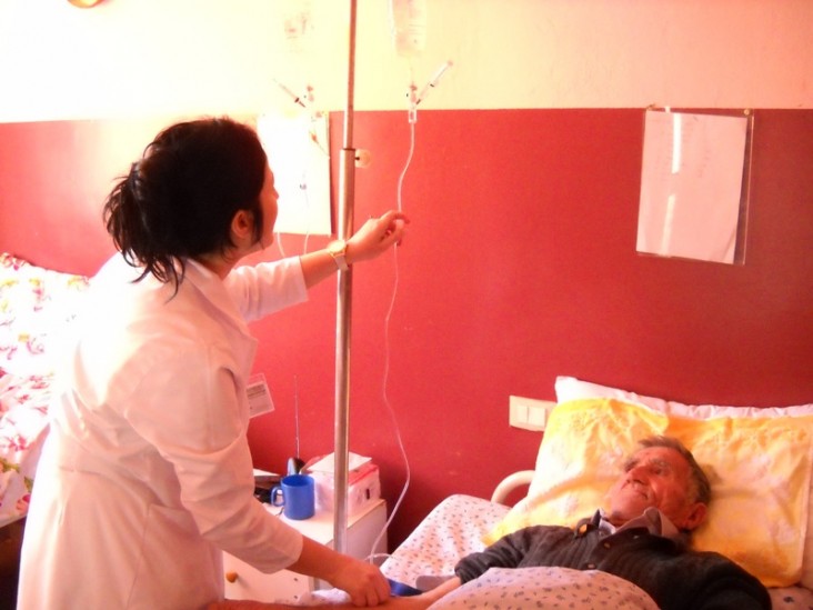 A nurse administers medication through an IV to a patient in a hospital bed