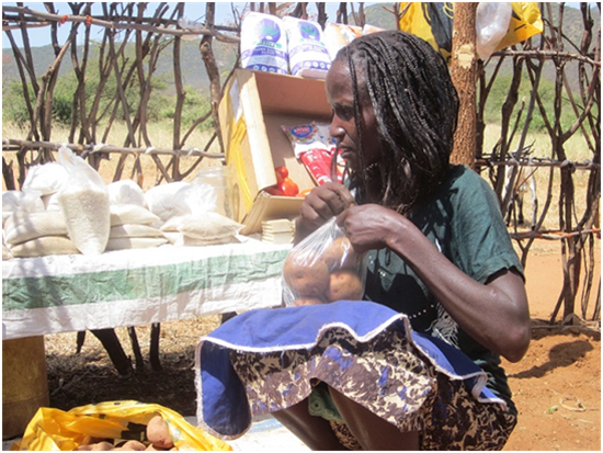 A woman kneels down while opening a bag of potatoes.