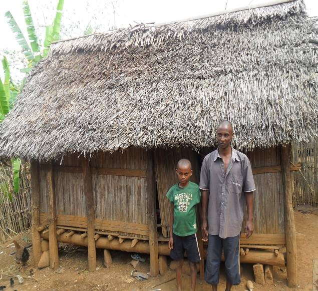 Rasolo and his son stand in front of their old home.