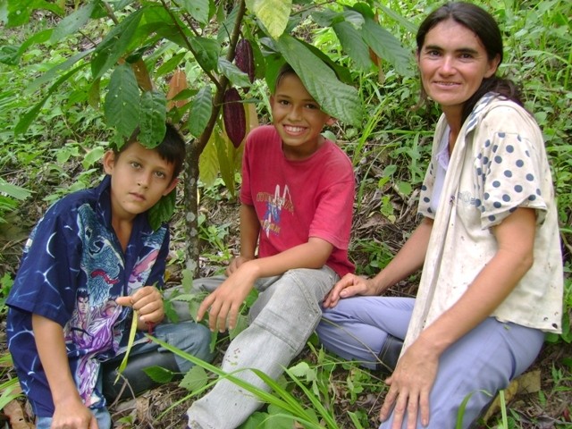 After her husband was murdered and she was threatened, “Maria” (with her two sons in a cacao plantation) welcomed a chance to le