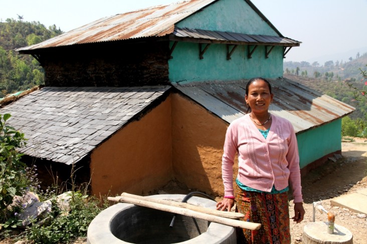 A woman stands next to a waste pit, installed with biogas technology, in front of her home.