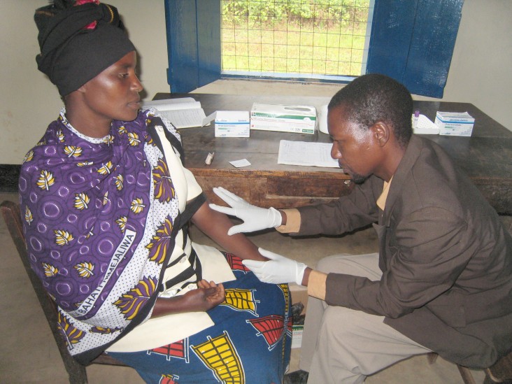 Government health worker Frank Mputa prepares to collect a blood sample from a local woman during a voluntary counseling and tes