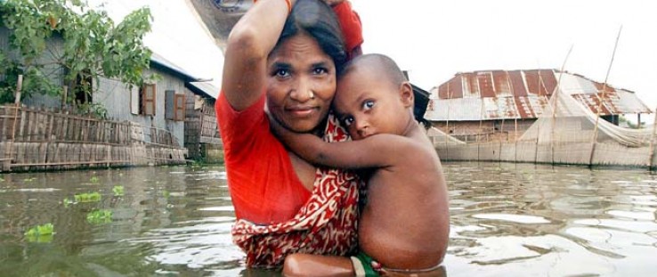 A mother carries her child in one hand and a packet of collected food in the other down a flooded road on the outskirts of Dhaka