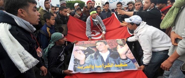 Tunisians from the Kasserine region walk with a Mohammed Bouazizi poster and the national flag in front of the government palace