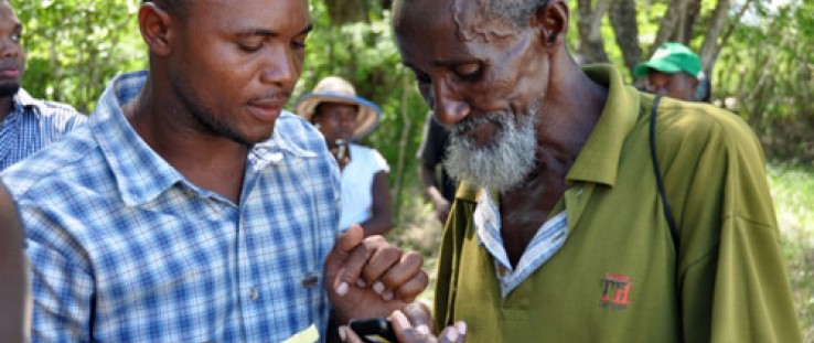 The man on the left explains how to use mobile money in Haiti's Pandiassou community as part of a USAID grant to Mercy Corps.