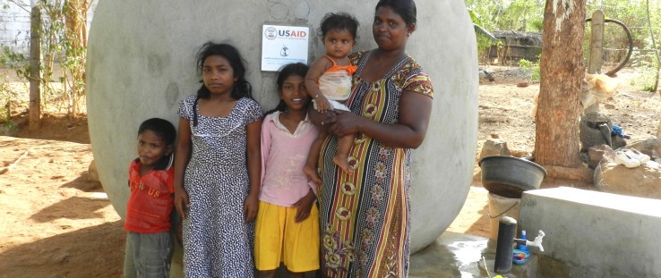 A family stands in front of their rainwater harvesting tank.
