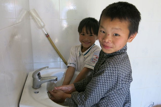 Two children wash their hands in a bathroom sink
